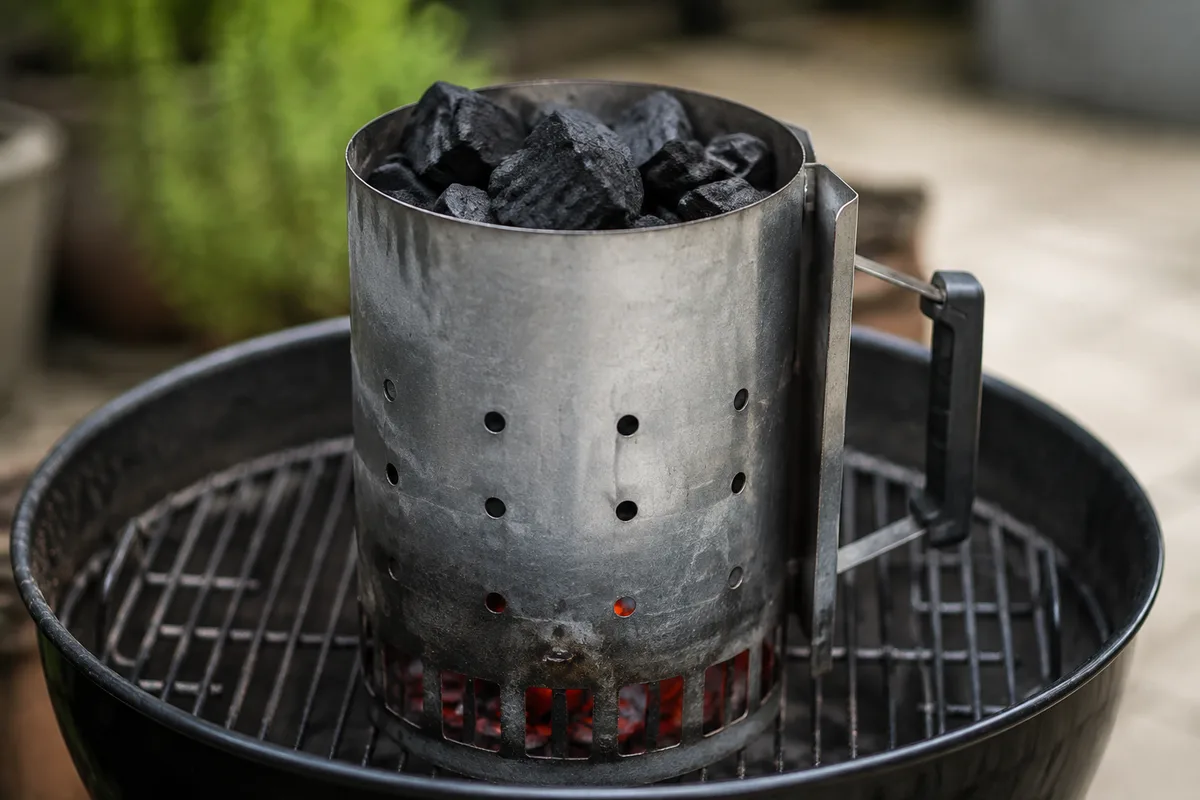 Charbon de bois en morceaux versé dans une cheminée d’allumage métallique posée sur une grille