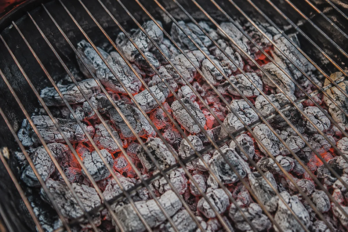 Braises recouvertes de cendre grise réparties dans la cuve d’un barbecue, grille posée au-dessus