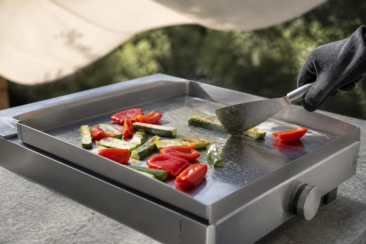 Plancha en inox posée sur un plan de travail extérieur en pierre à côté d&rsquo;une terrasse ombragée