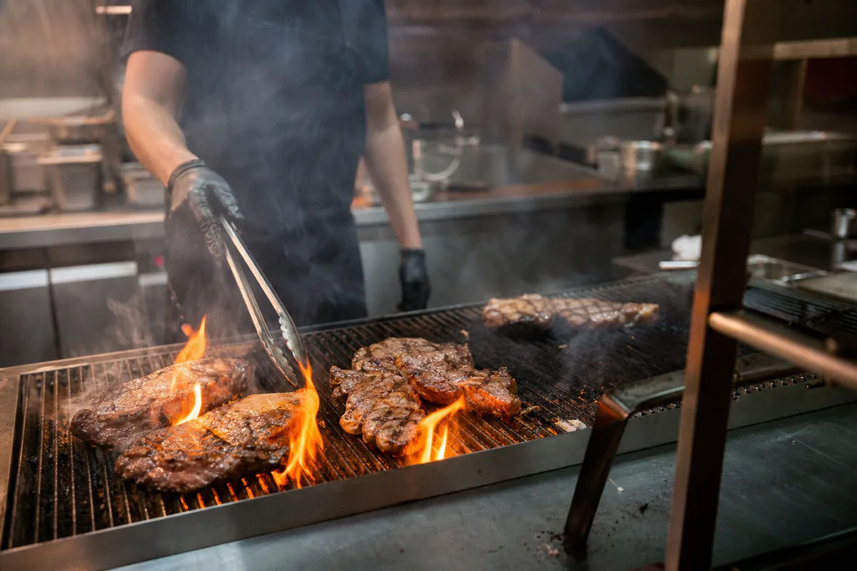 Grillardin surveillant la cuisson de viandes sur un grand gril professionnel
